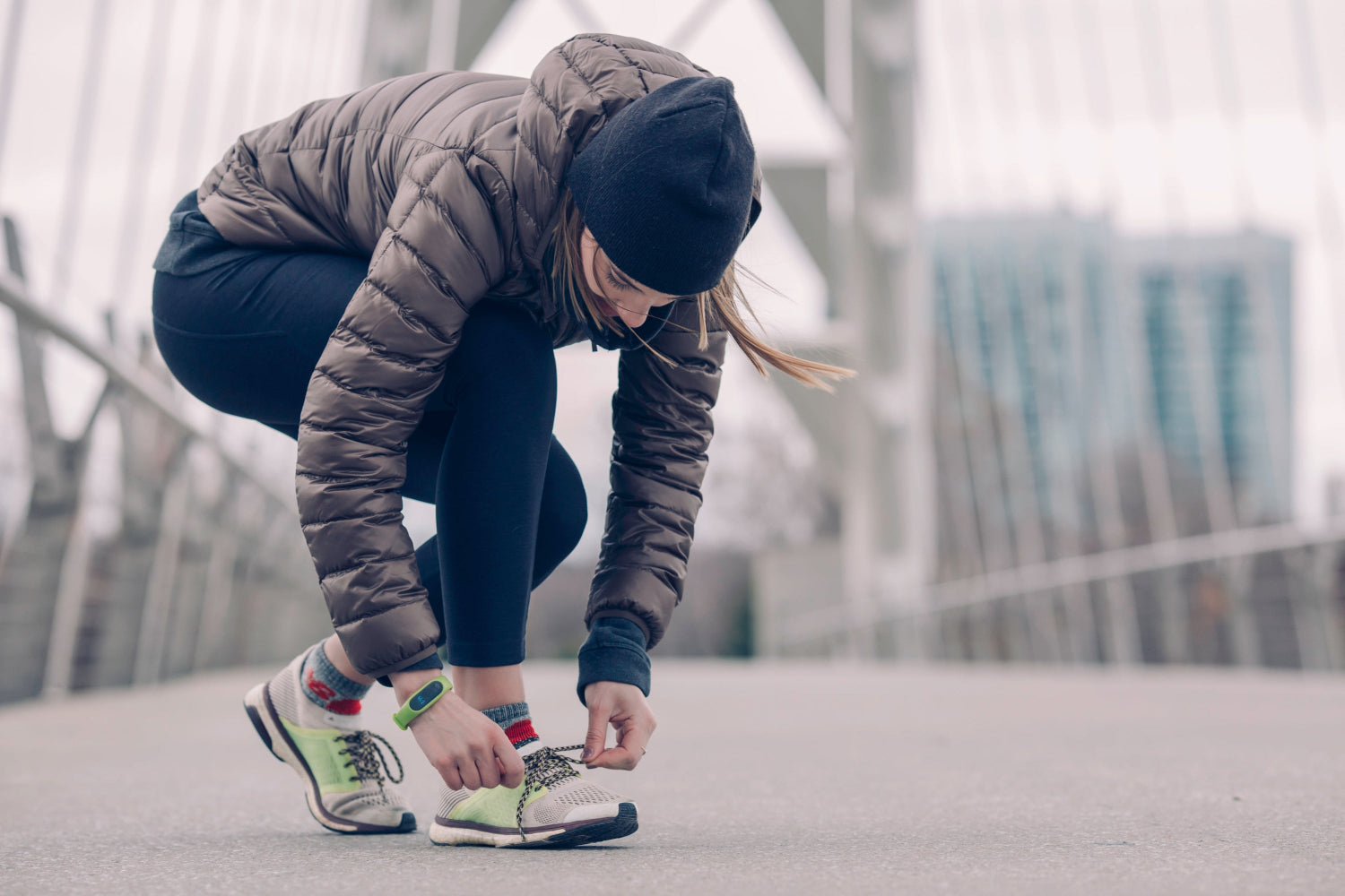 Person in winter clothing tying running shoes on a bridge